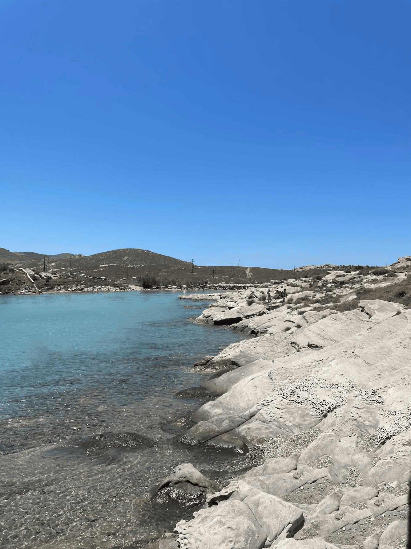 Scenic view of Paros island's rocky coast, calm waters, and bright blue sky, perfect for relaxing se.
