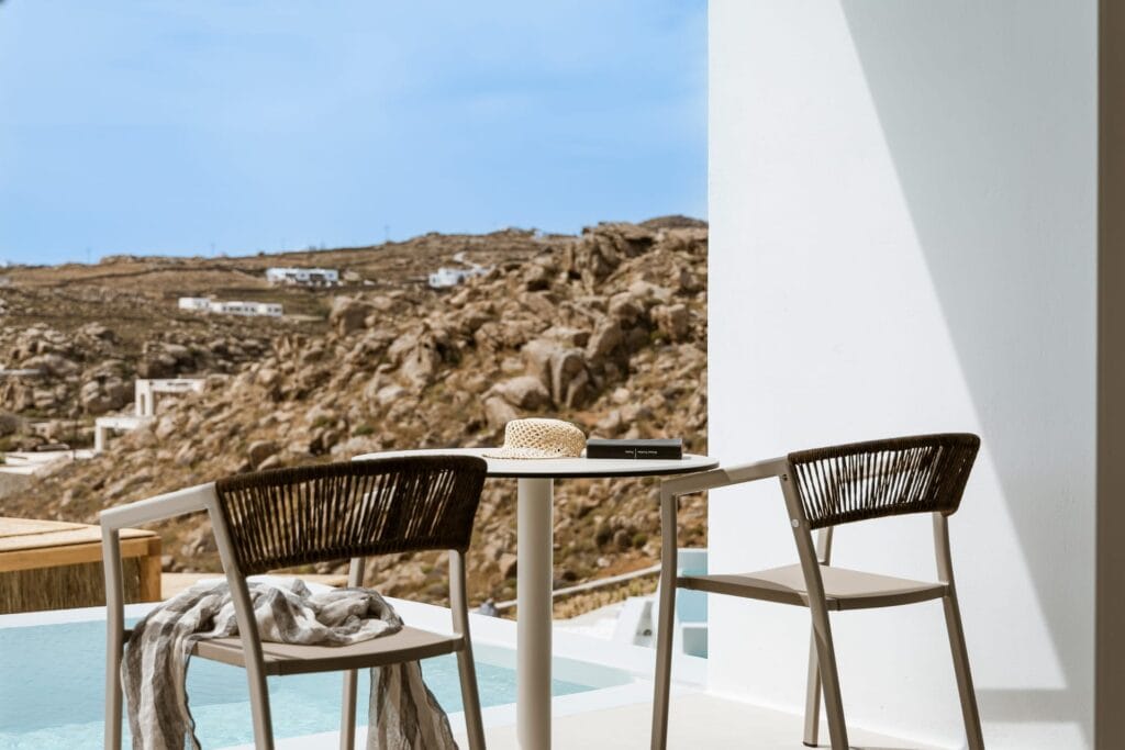 Pool suite with side sea view, outdoor seating, and scenic Cyclades landscape.