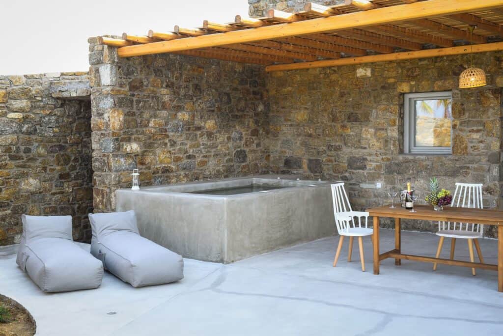 Modern master suite with plunge pool, outdoor seating, and stone wall in Cyclades, Greece.