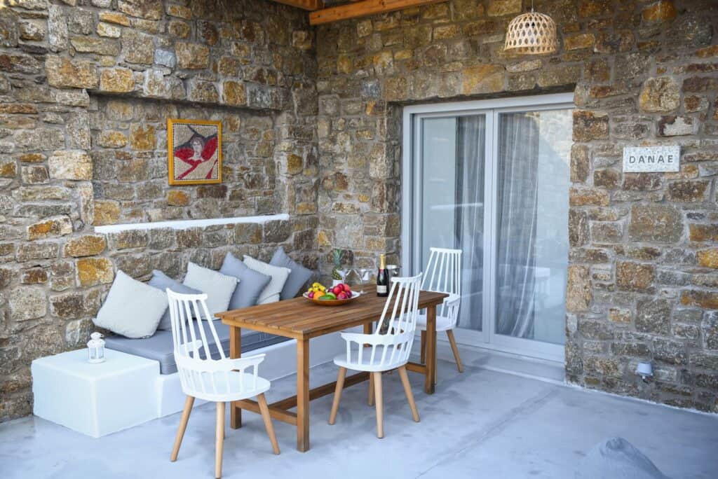 Outdoor dining space with stone wall, white chairs, and a wooden table, perfect for relaxing meals i.