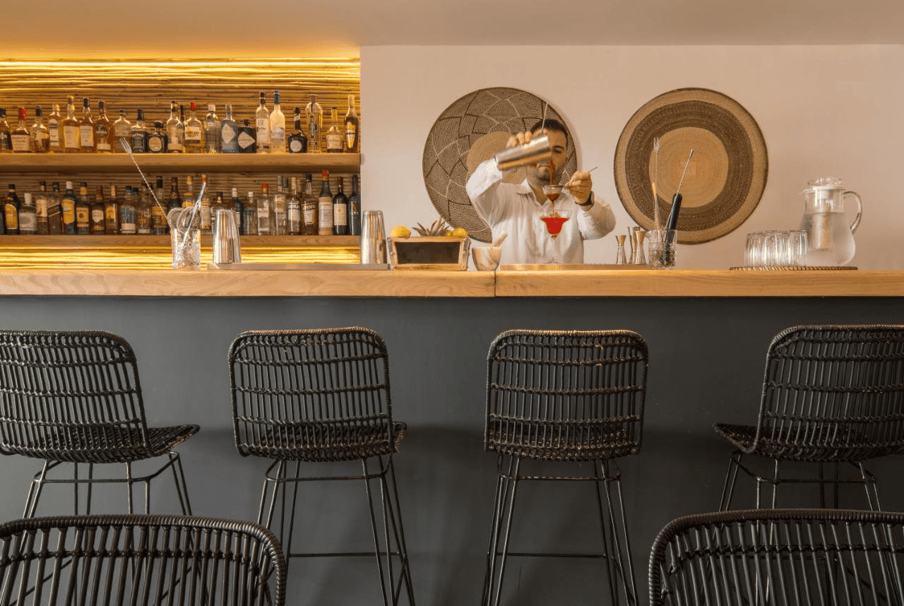 Stylish bar at Mykonos boutique hotel with modern decor and barista serving drinks.