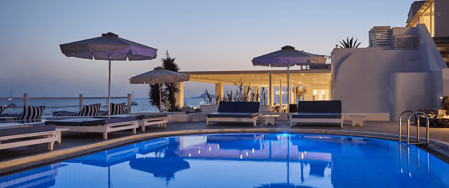 Pool area with sun loungers and umbrellas at Notos Therme and Spa, Cyclades, during sunset.