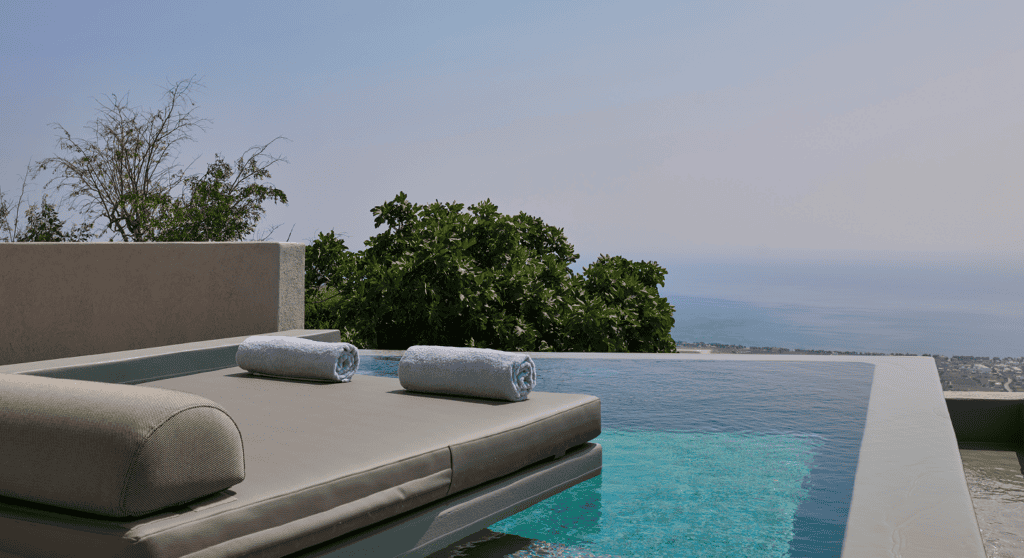Infinity pool overlooking the Aegean Sea with loungers and scenic landscape.