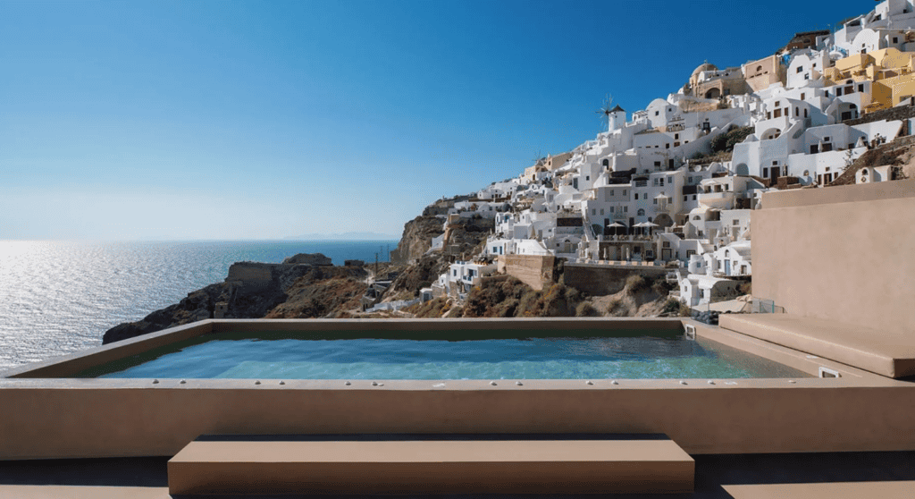 Infinity pool overlooking Old Castle Oia with white buildings and Aegean Sea view.