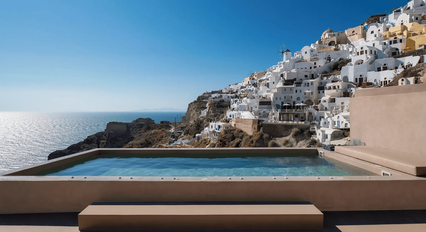 Infinity pool overlooking Old Castle Oia with white buildings and Aegean Sea view.