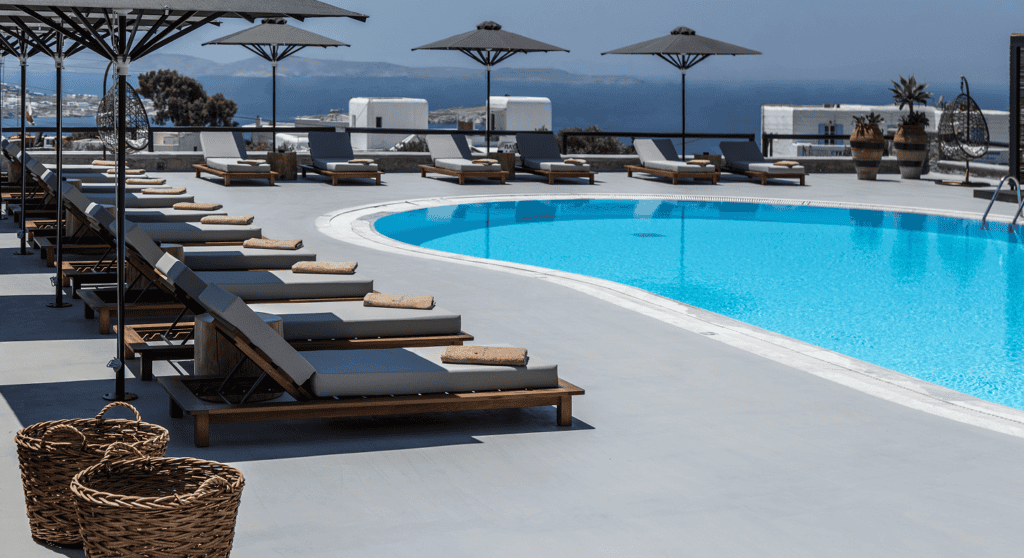Poolside lounge chairs and umbrellas at Mykonos boutique hotel with sea view.