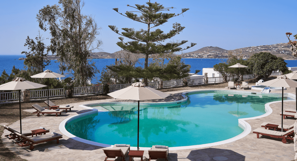 Scenic view of High Mill Paros with pool, trees, and sea in the background.