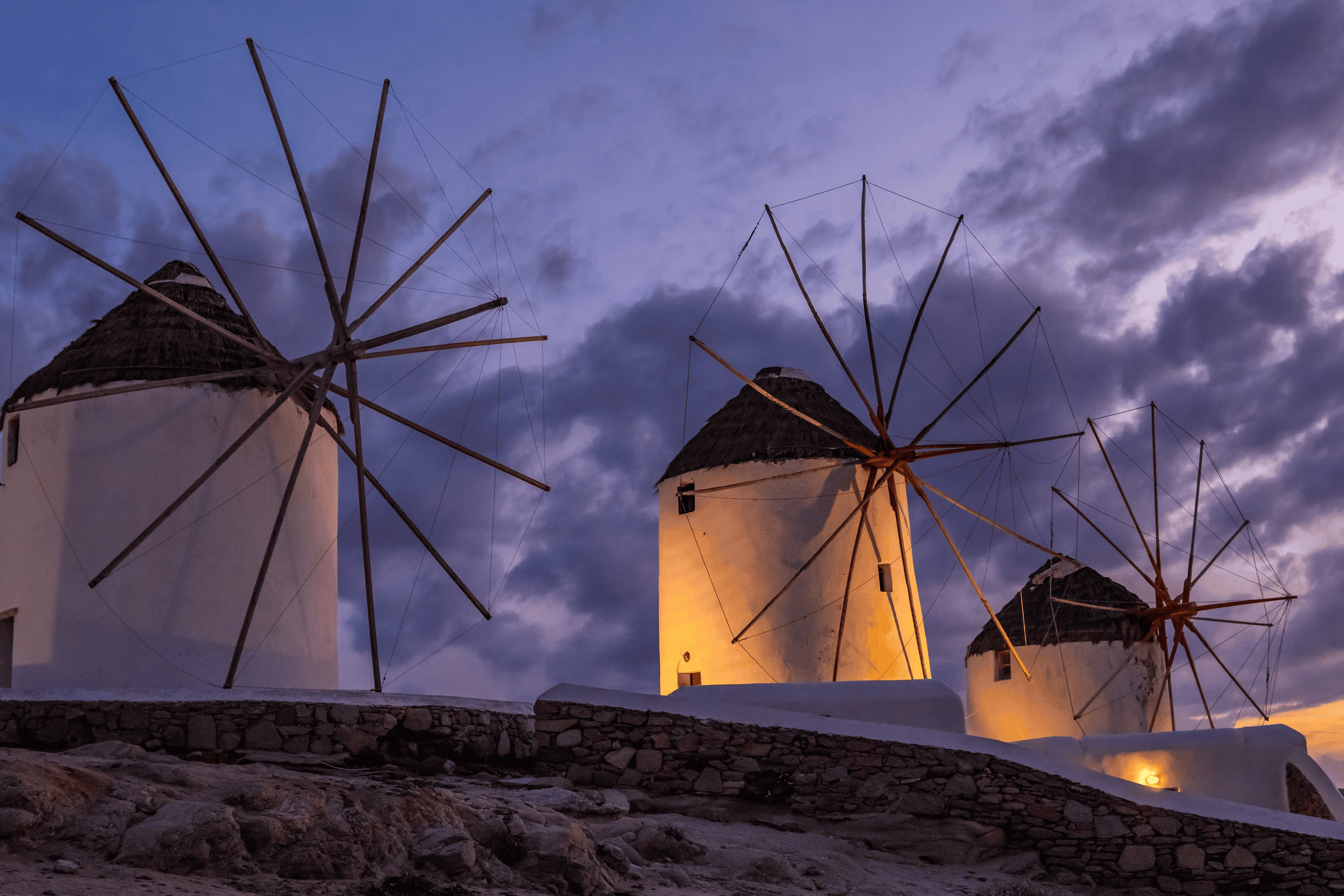 Mykonos windmills with illuminated bases against a dramatic evening sky. Iconic Greek landmarks near.