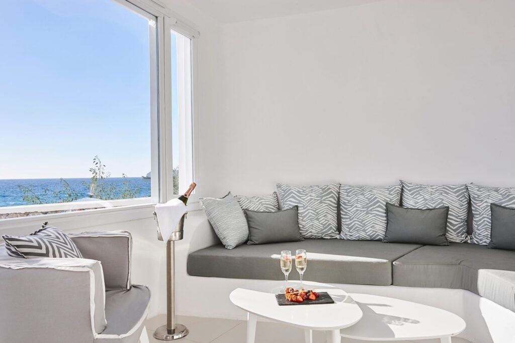 Sea view junior suite with modern decor and comfortable seating overlooking the Aegean Sea.